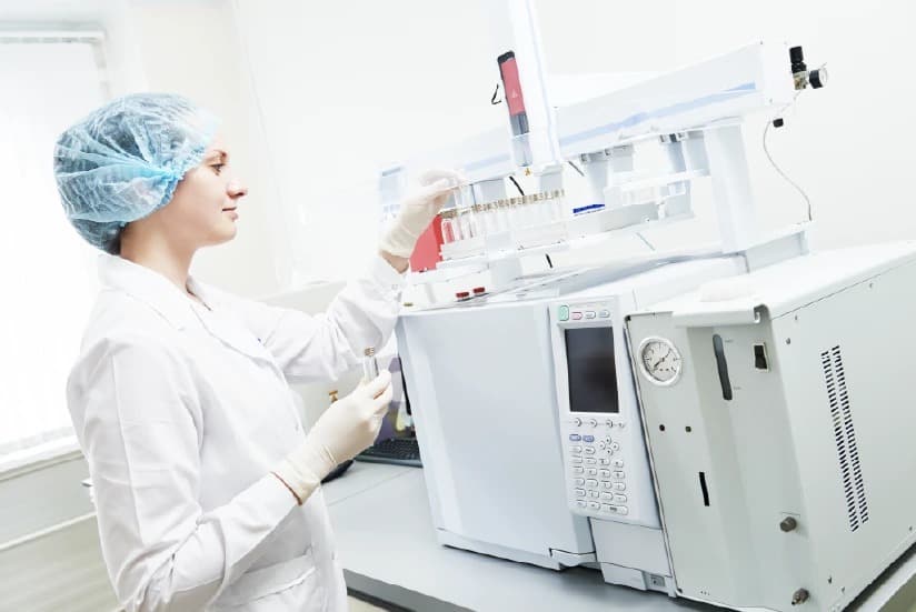 Scientist handling laboratory equipment wearing a lab coat and protective cap.