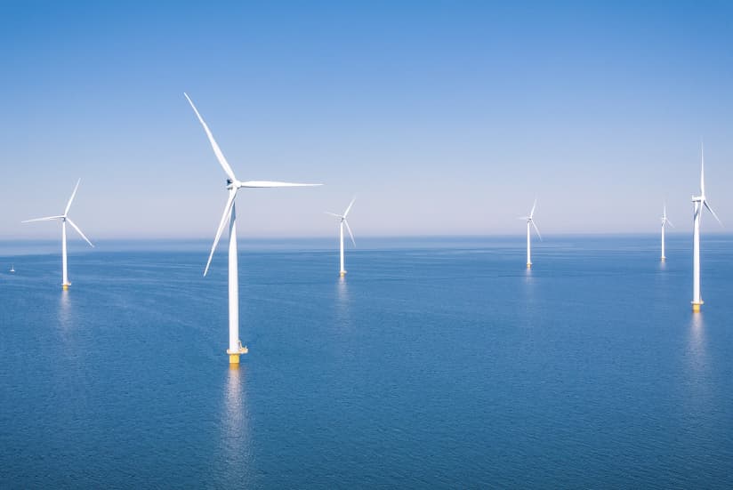 White wind turbines on an offshore wind farm under a clear blue sky.