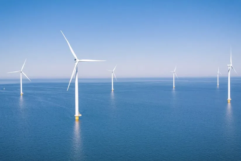 White wind turbines on an offshore wind farm under a clear blue sky.